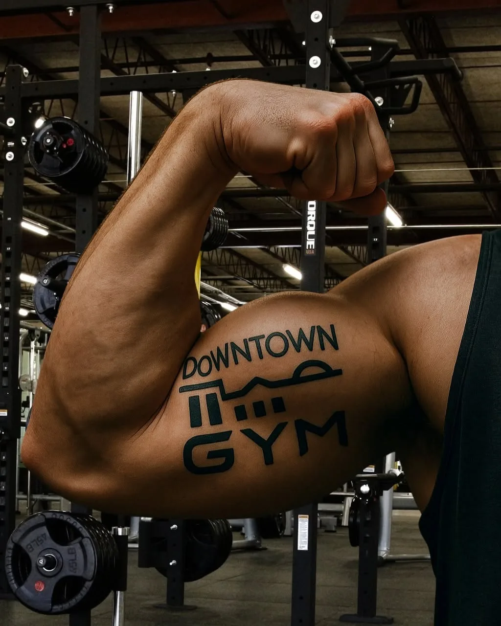 Downtown Gym member flexing a bicep tattoo of the gym logo
