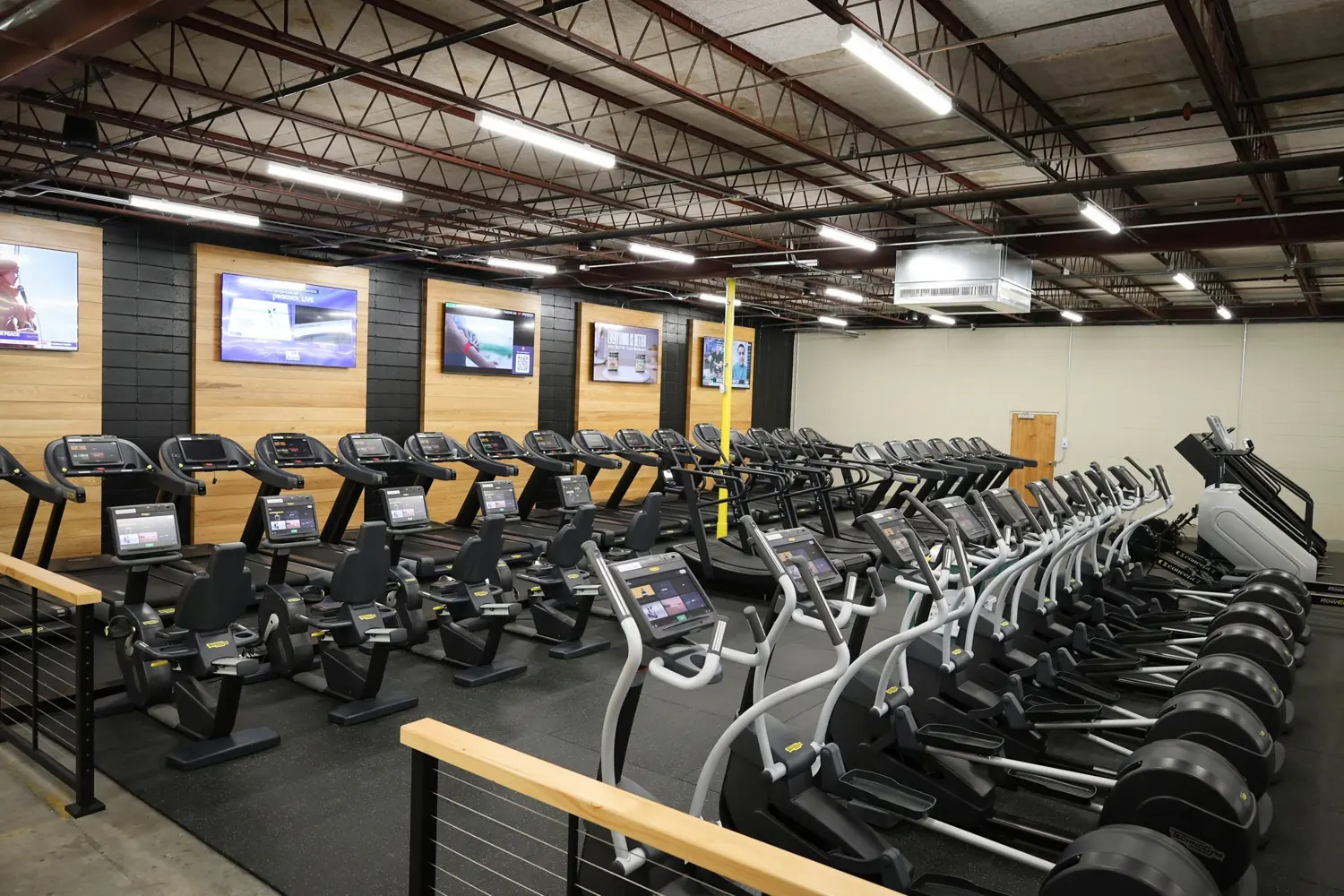 A row of cardio machines facing wall-mounted TVs